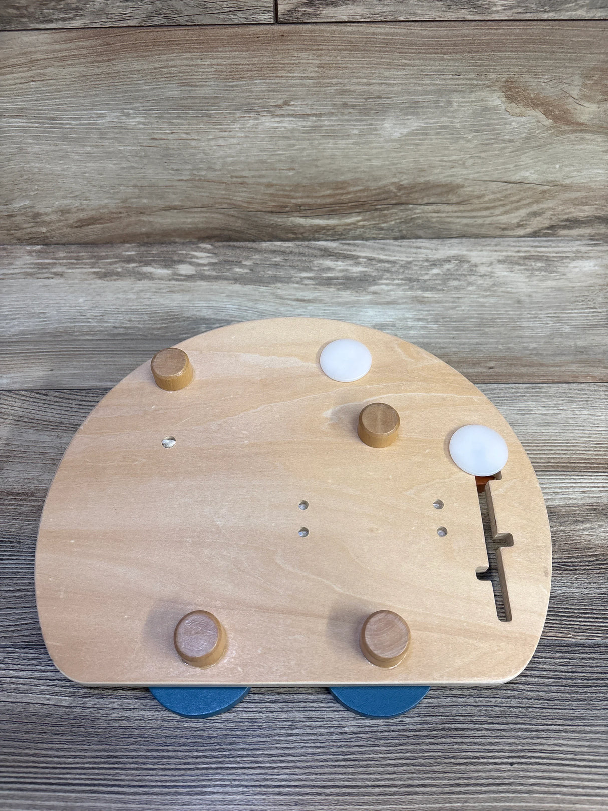Top-down view of Classic World Fire Engine busy board showing four wooden knobs, two white push buttons, a sliding latch and blue wheel accents on a wood background