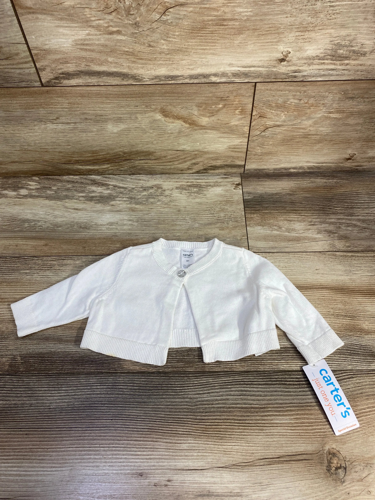 White long-sleeve baby cardigan with a single button and carter's clothing tag on wood floor