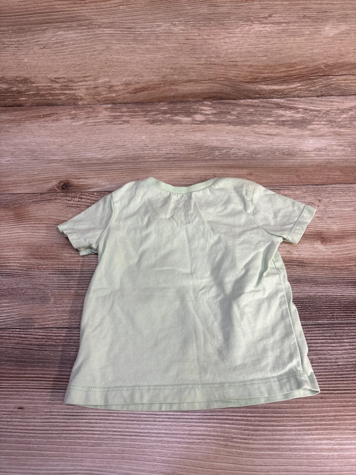 Front view of Honest Baby solid green shirt showcasing short sleeves with a wood-grain background
