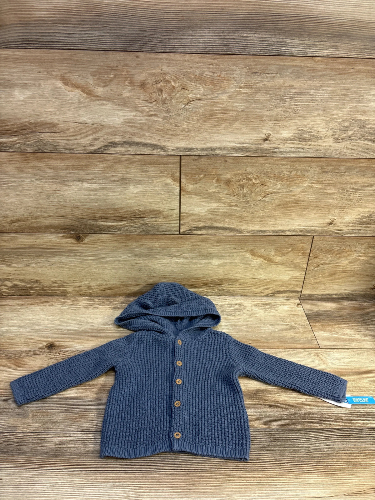 Front view of navy blue knit hooded cardigan showcasing wooden buttons and textured knit on a wood background