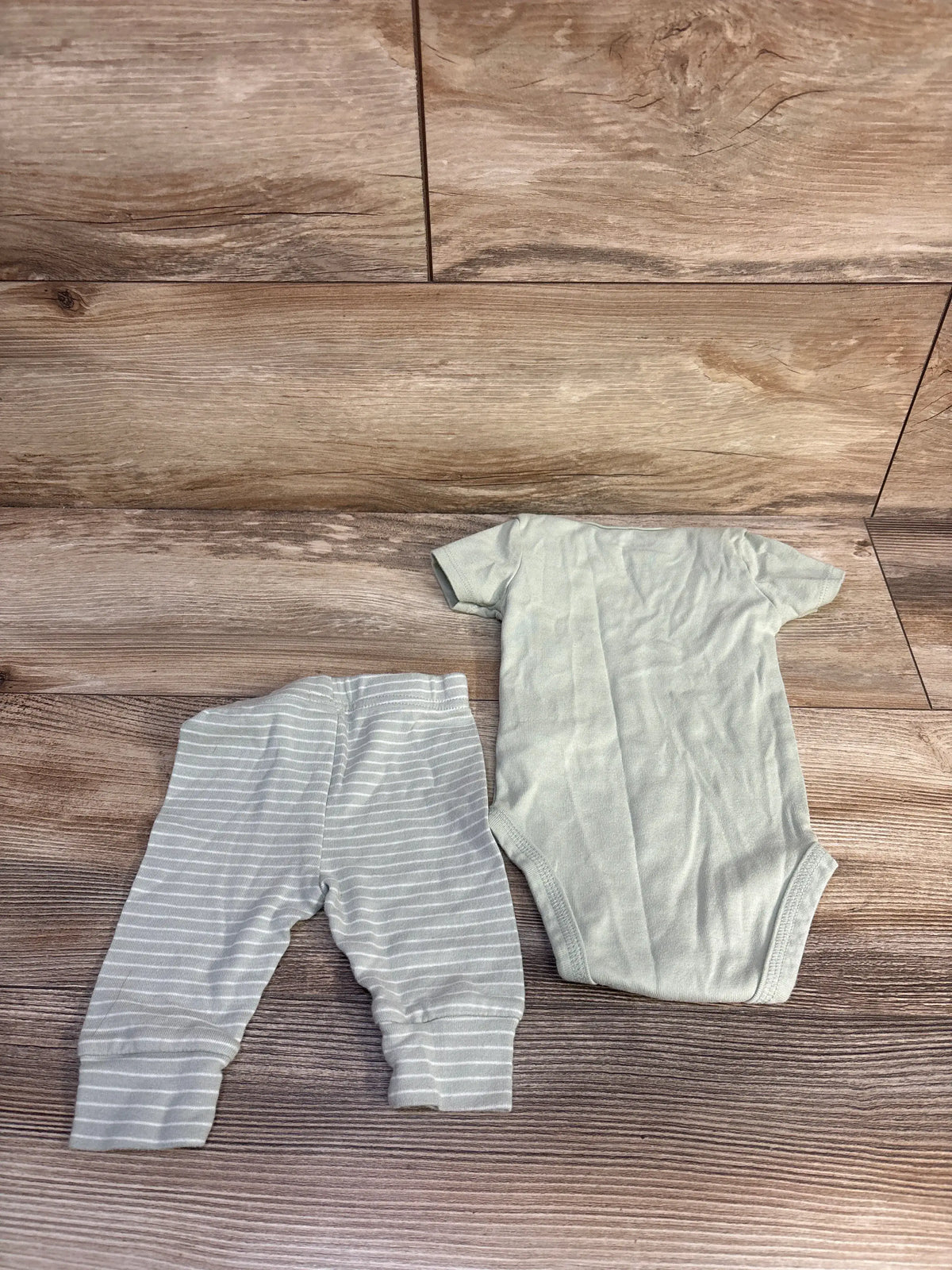 Top view of Just One You 2-piece bodysuit and pants set showcasing a green bodysuit and striped pants on wood