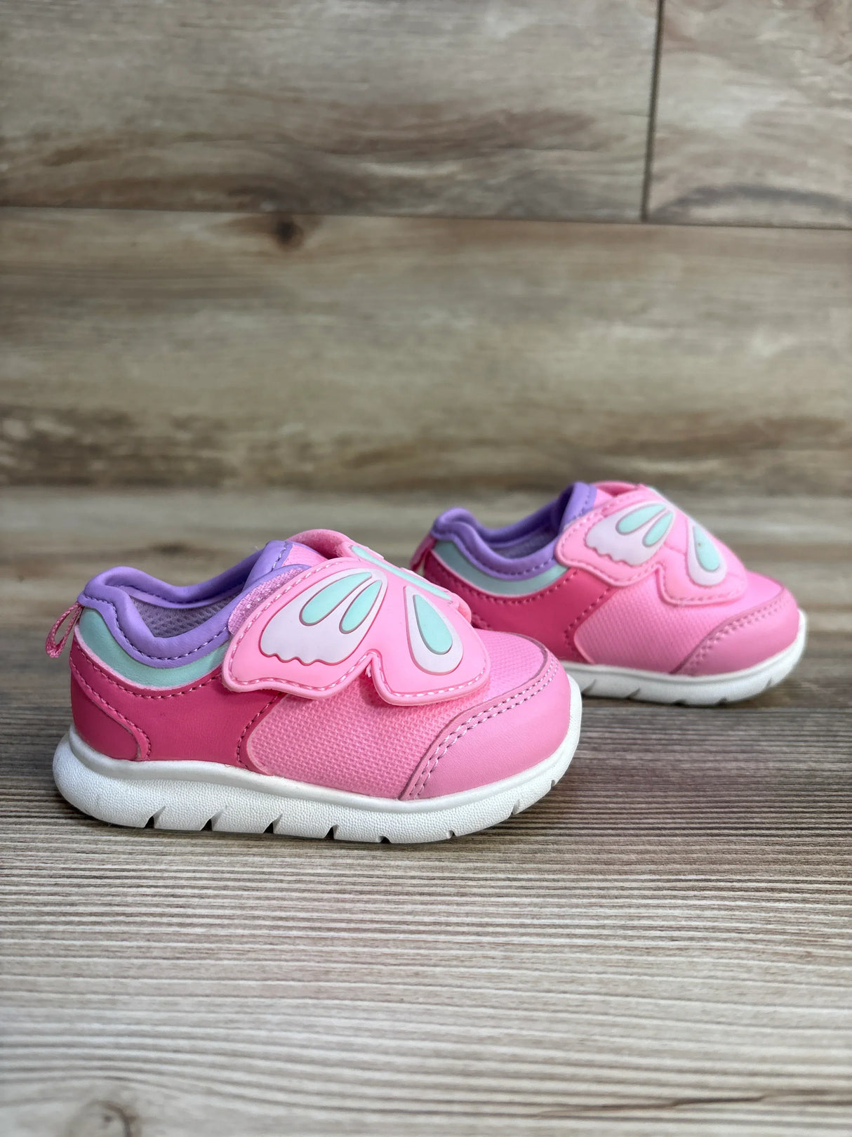 Pink toddler sneakers with butterfly wing design and white soles on wood floor