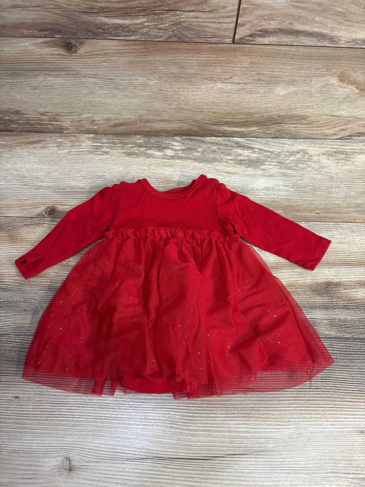 Red long sleeve baby dress with tulle skirt and glitter details, laid on wood floor