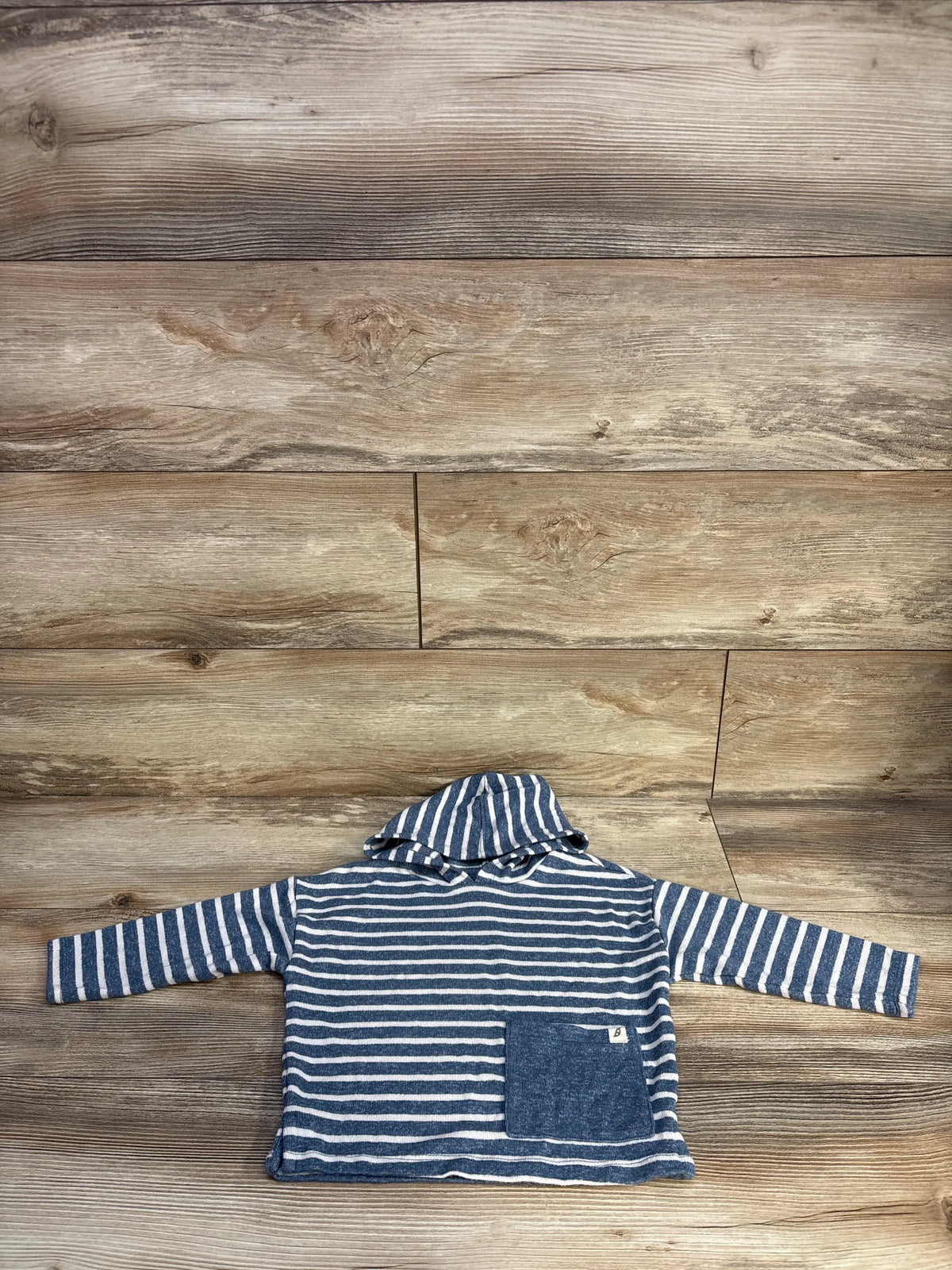 Front view of Easy Peasy striped hooded shirt showcasing blue and white stripes and front pocket on wood background