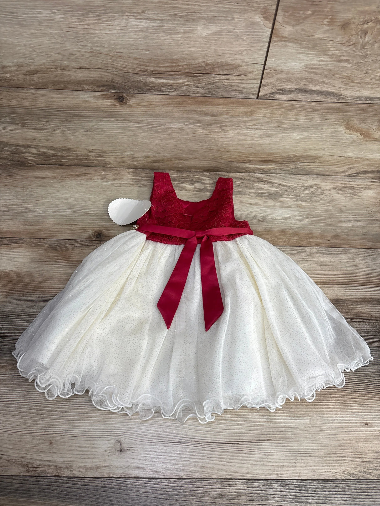 Baby girl's sleeveless dress with red lace bodice and white tulle skirt with bow, on wood floor