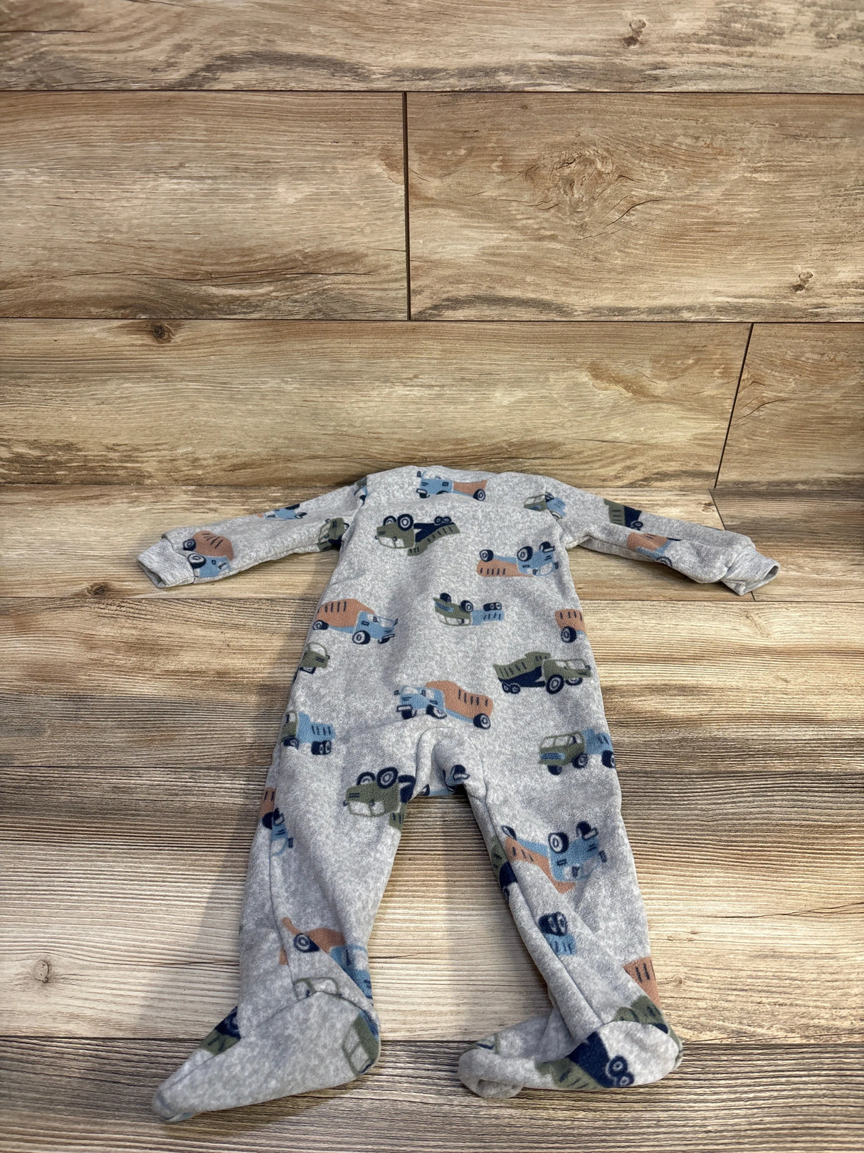 Flat lay of Carter’s blanket sleeper in grey showing all-over truck print and footed design on wood background