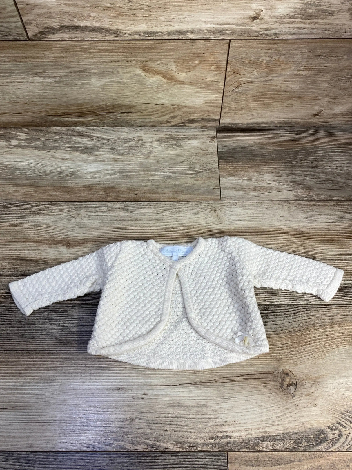 Cream knit baby cardigan with textured pattern on wood background