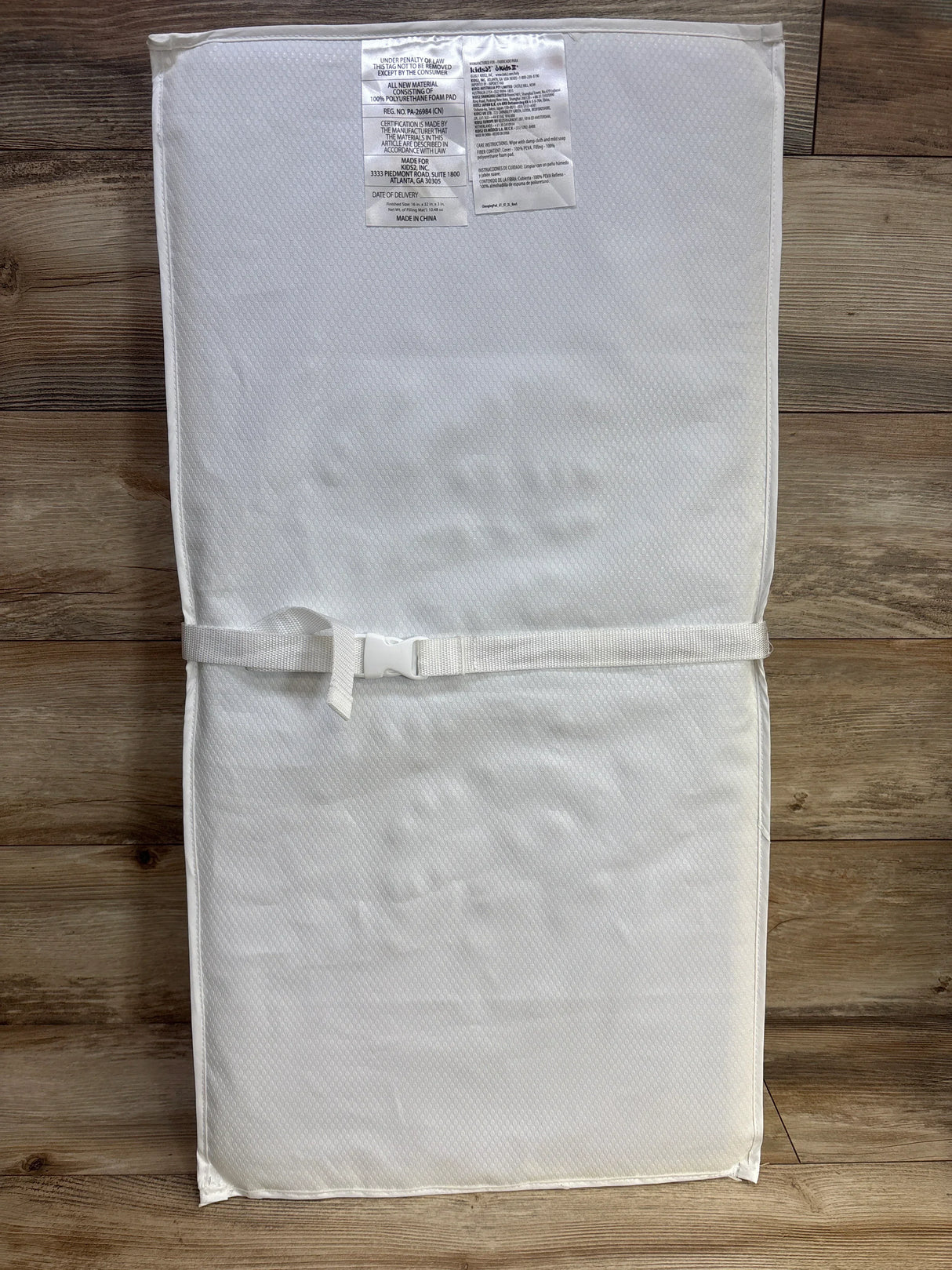 White contoured baby changing pad with safety strap on wood floor, nursery accessory