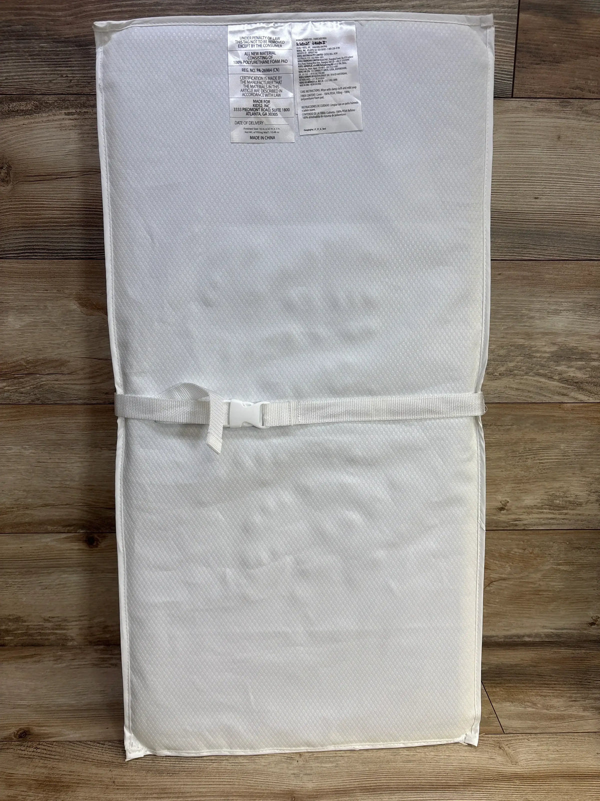 White contoured baby changing pad with safety strap on wood floor, nursery accessory