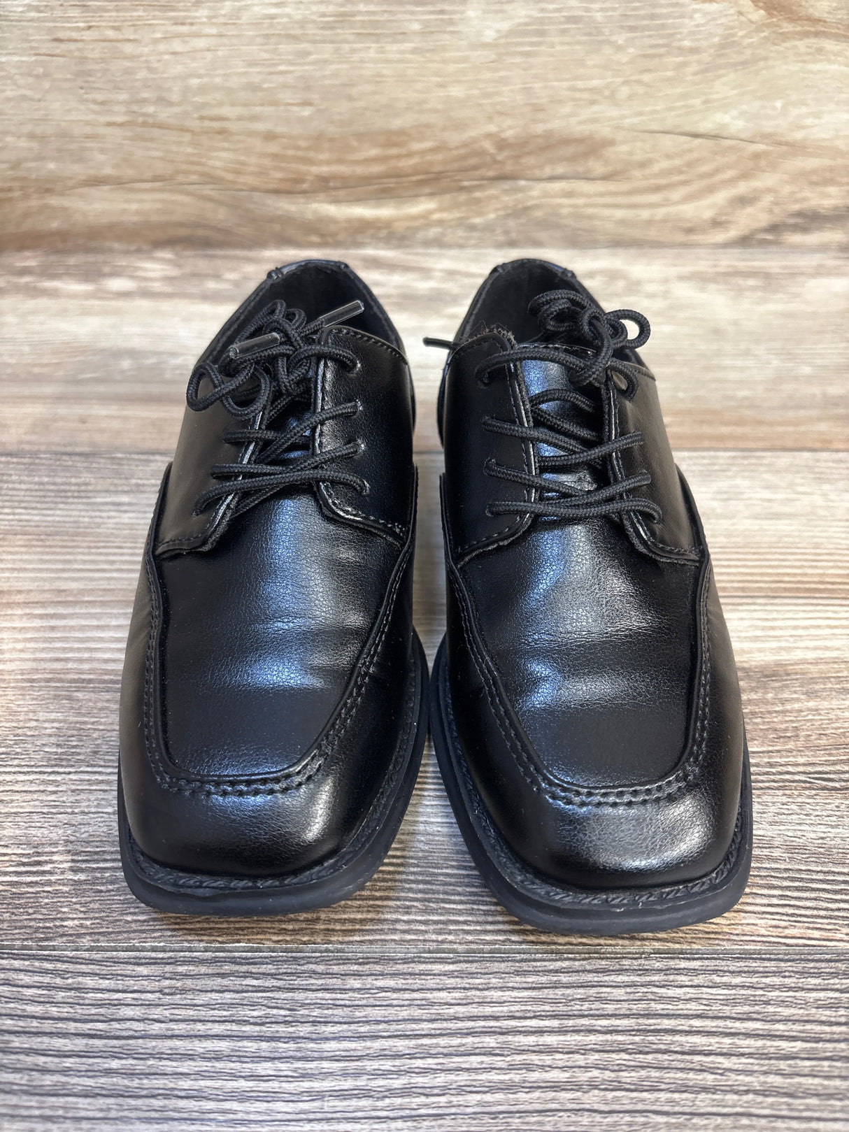 Pair of black leather youth dress shoes with laces on wooden background
