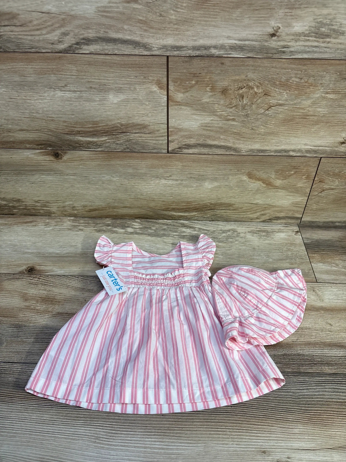 Top view of a pink and white striped baby dress and matching bloomers with gathered waist and ruffled sleeves on wood flooring