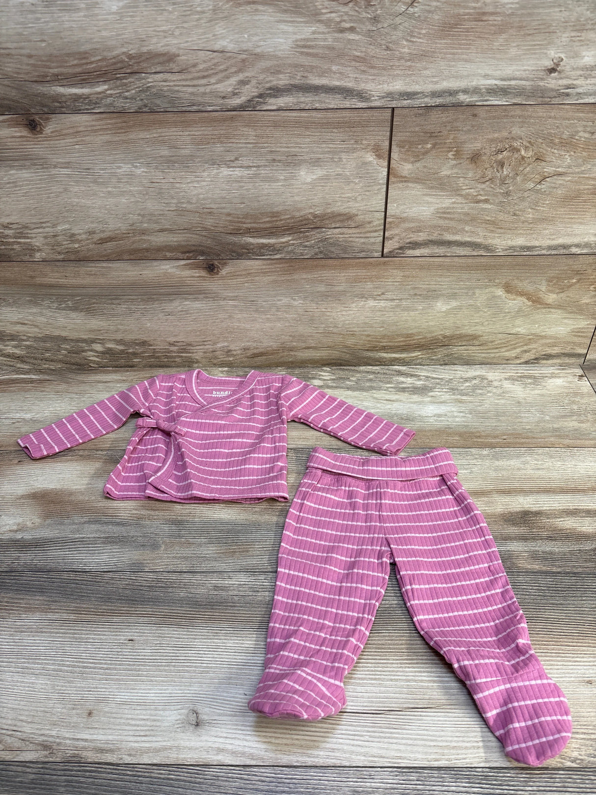 Top-down view of pink striped kimono shirt and matching footed pants set with side tie and footed bottoms on wood background