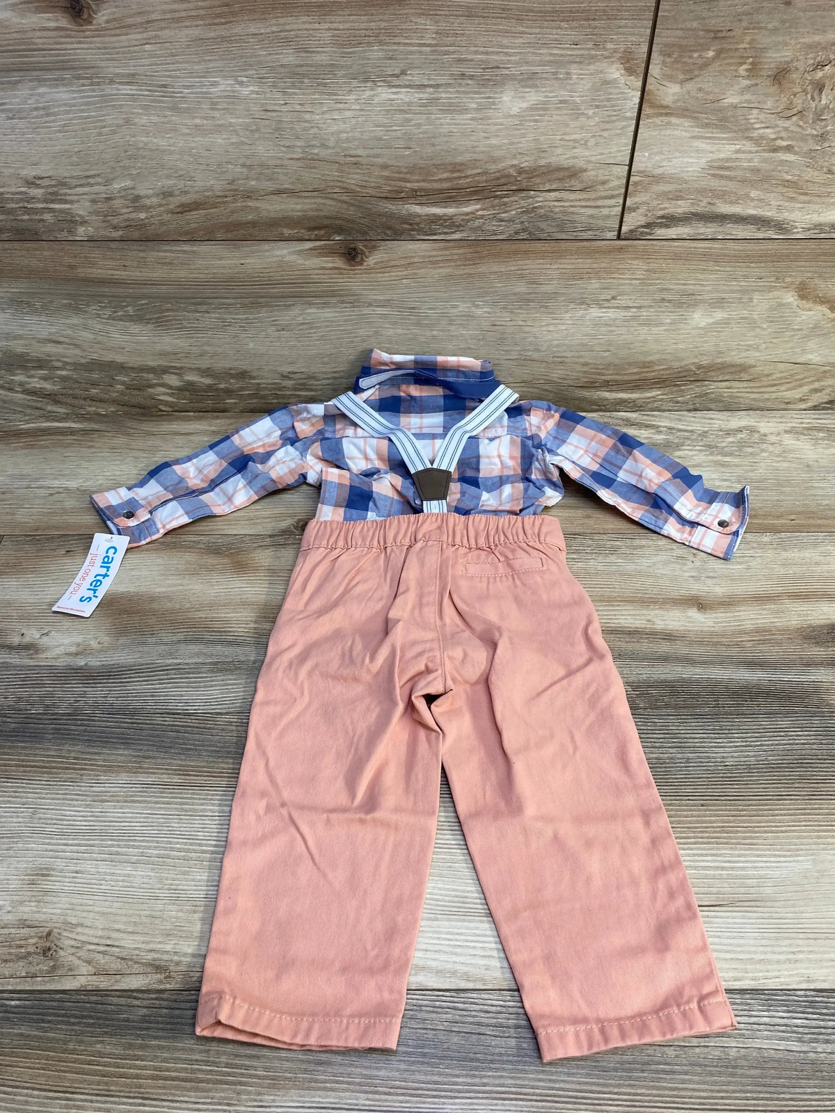 Flat lay of 4-piece baby plaid button-up shirt with striped suspenders and peach pants, size 12 months on wood background