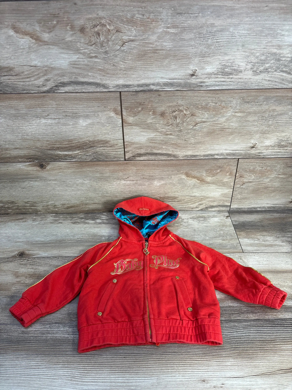 Front view of Baby Phat vintage zip-up hoodie in red with gold logo, blue patterned hood lining, and zip front