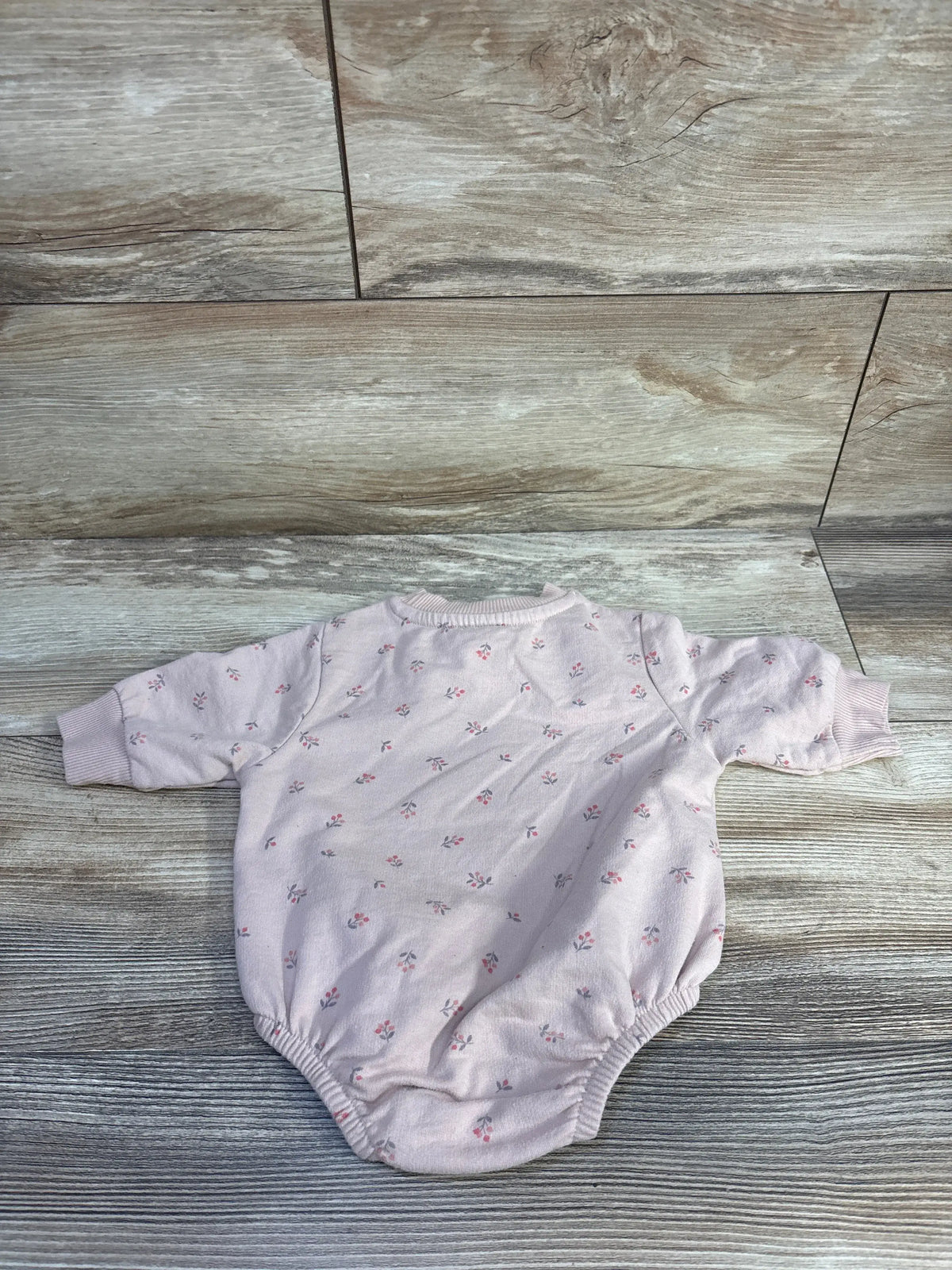 Flat lay of pink baby bubble romper showing long sleeves, elastic leg openings, and small floral print on wood background