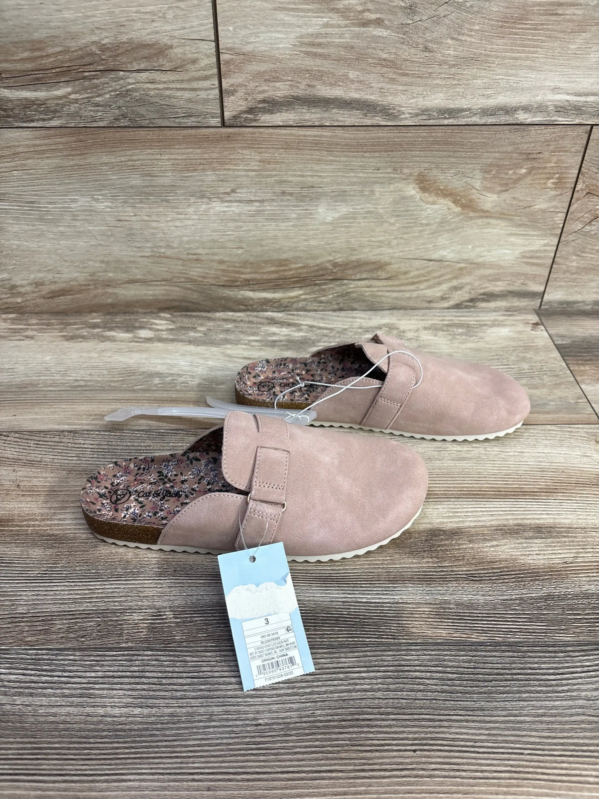 Pair of pink toddler slip-on shoes with floral insole and adjustable strap on wood flooring