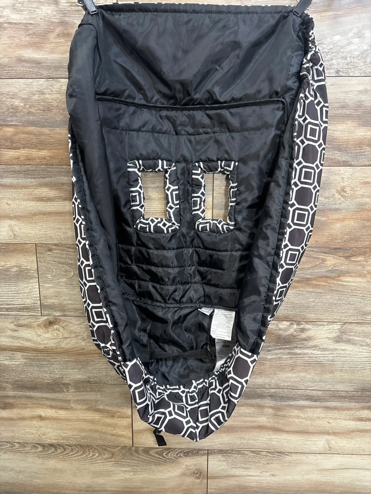 Flat lay of Boppy shopping cart and high chair cover showcasing black and white geometric trim with quilted seat and dual safety strap slots on wood plank floor