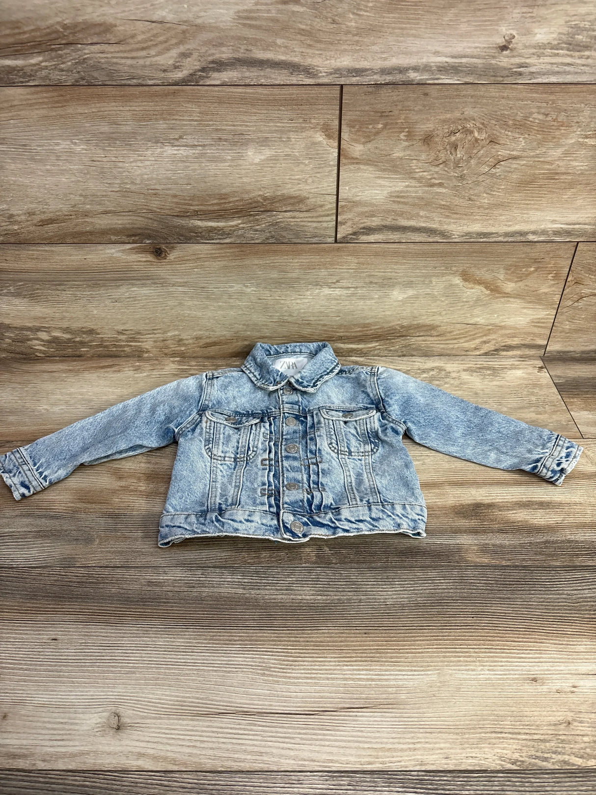 Light blue denim toddler jacket with buttons and chest pockets on wooden background