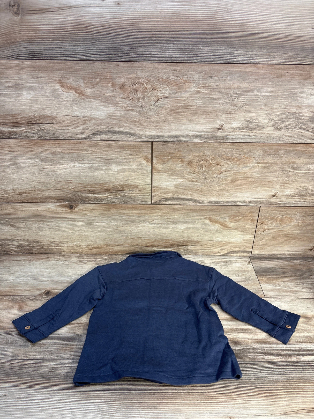 Navy blue long sleeve shirt with buttons, laid flat on wooden floor background