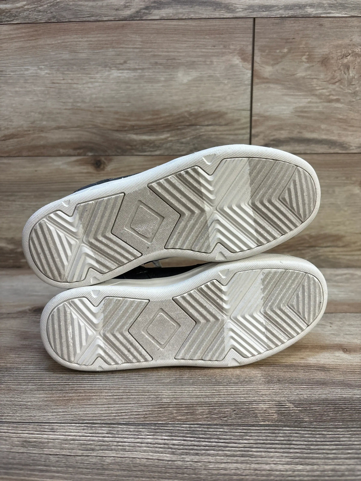 Bottom view of grey high top sneakers showing white rubber soles with geometric tread on wood floor