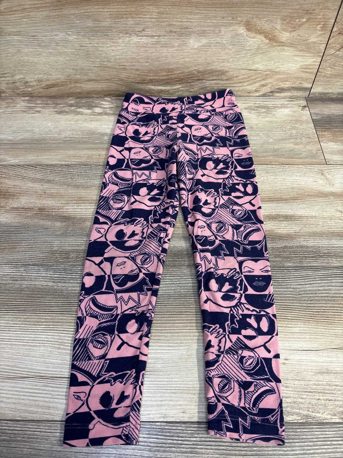 Flat lay of toddler Lularoe Evil Queen leggings showcasing all-over navy comic face print on a light wood floor