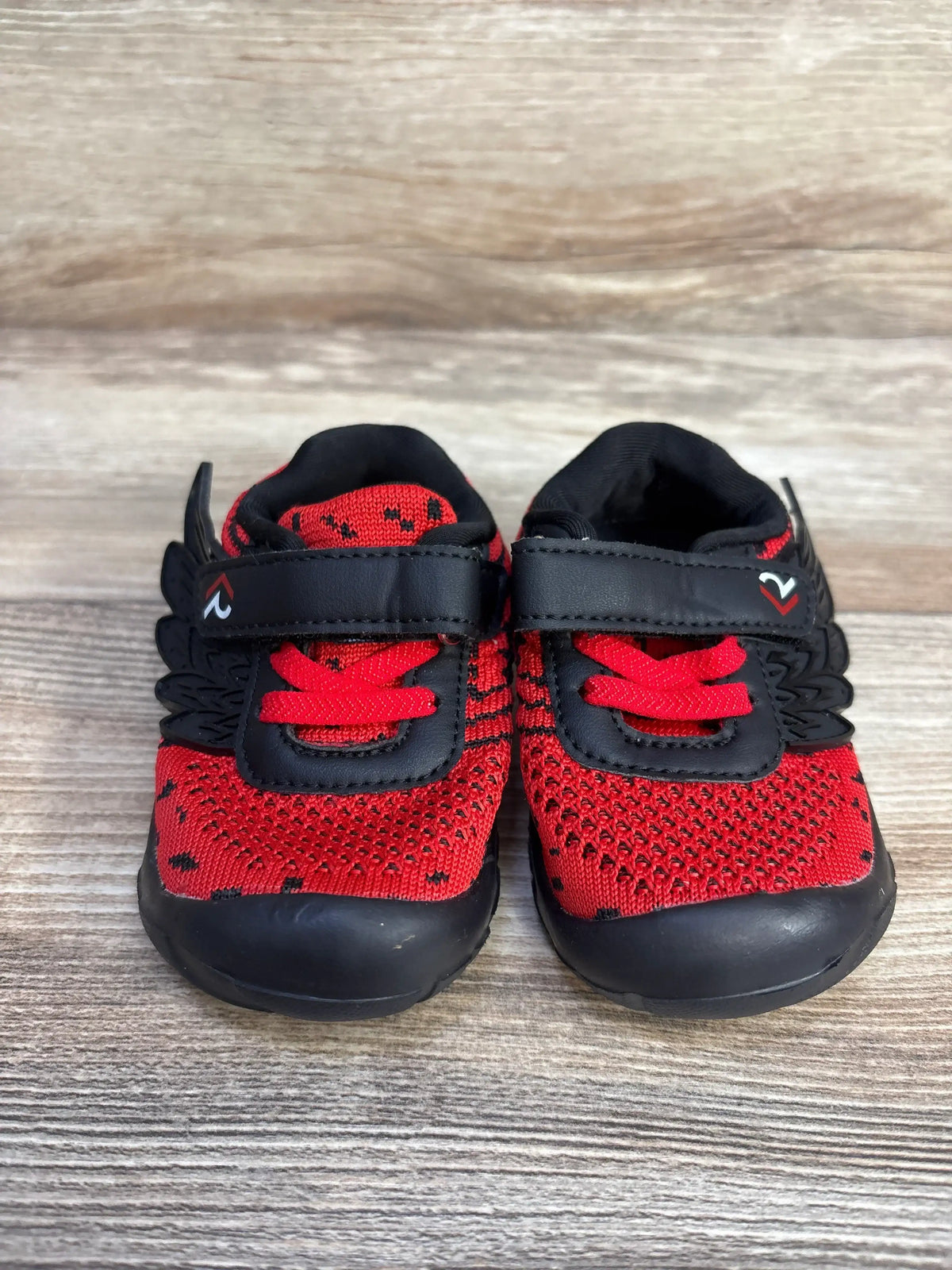 Front view of boy's red and black wing sneakers size 3.5C with knit upper and Velcro strap on wood background