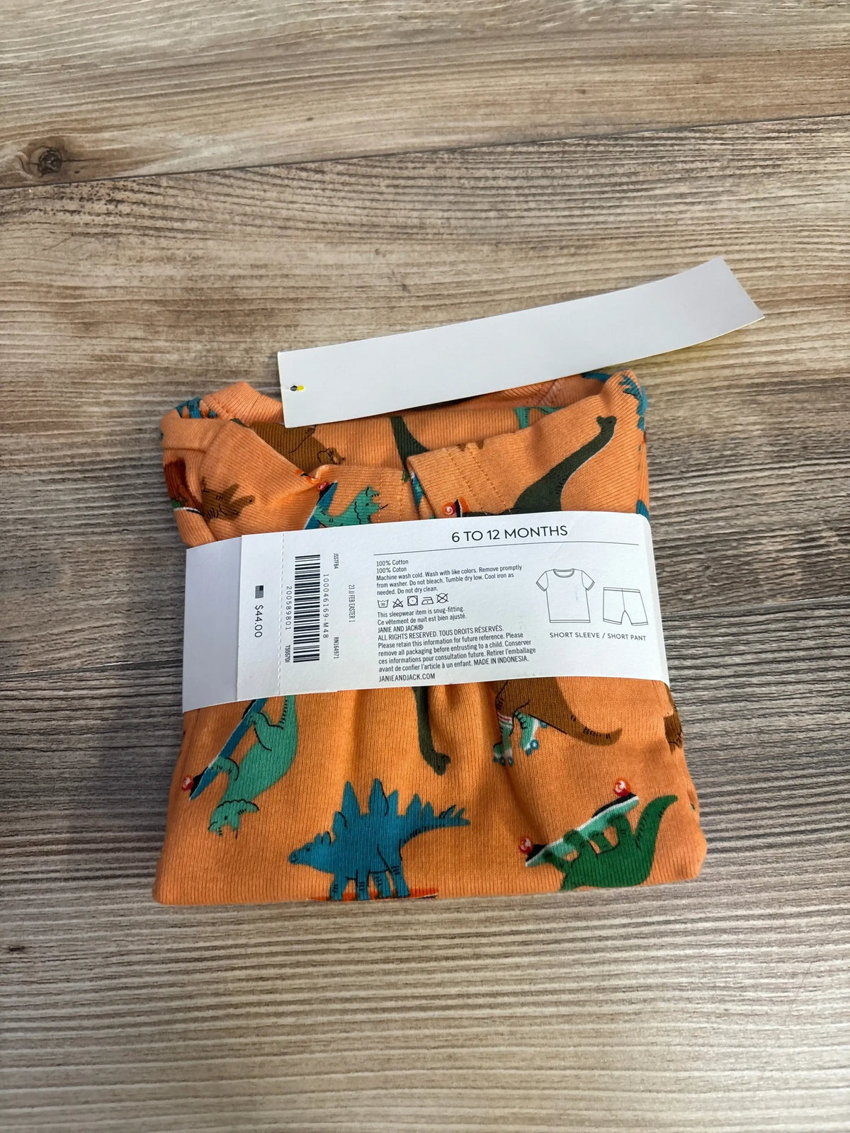 Folded orange baby pajamas with colorful dinosaur print, size 6 to 12 months, on wooden surface