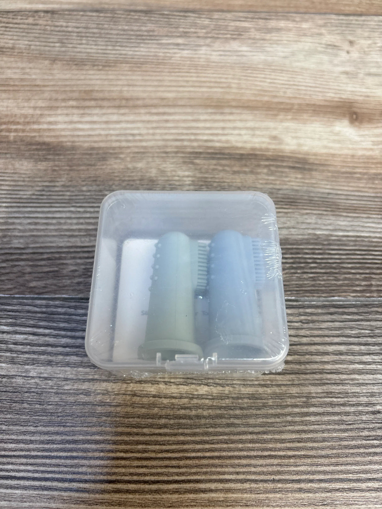 Two silicone baby finger toothbrushes in a clear case on wood surface
