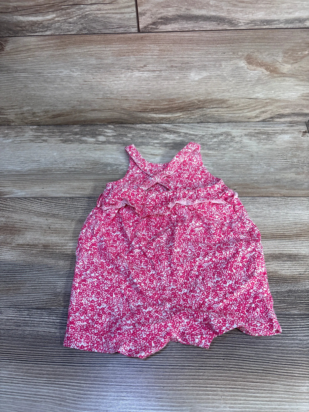 Front view of Carter’s pink shortie romper in size 6 months showcasing floral print and ruffled detail on a wood background