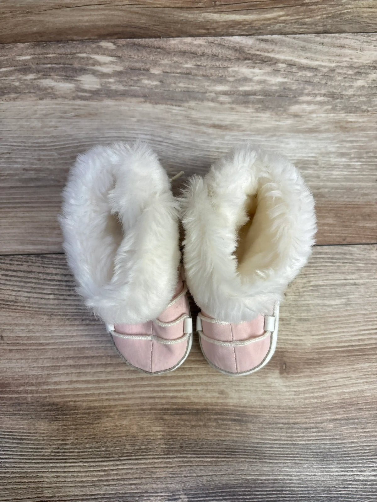 Pink baby booties with white faux fur on wood background
