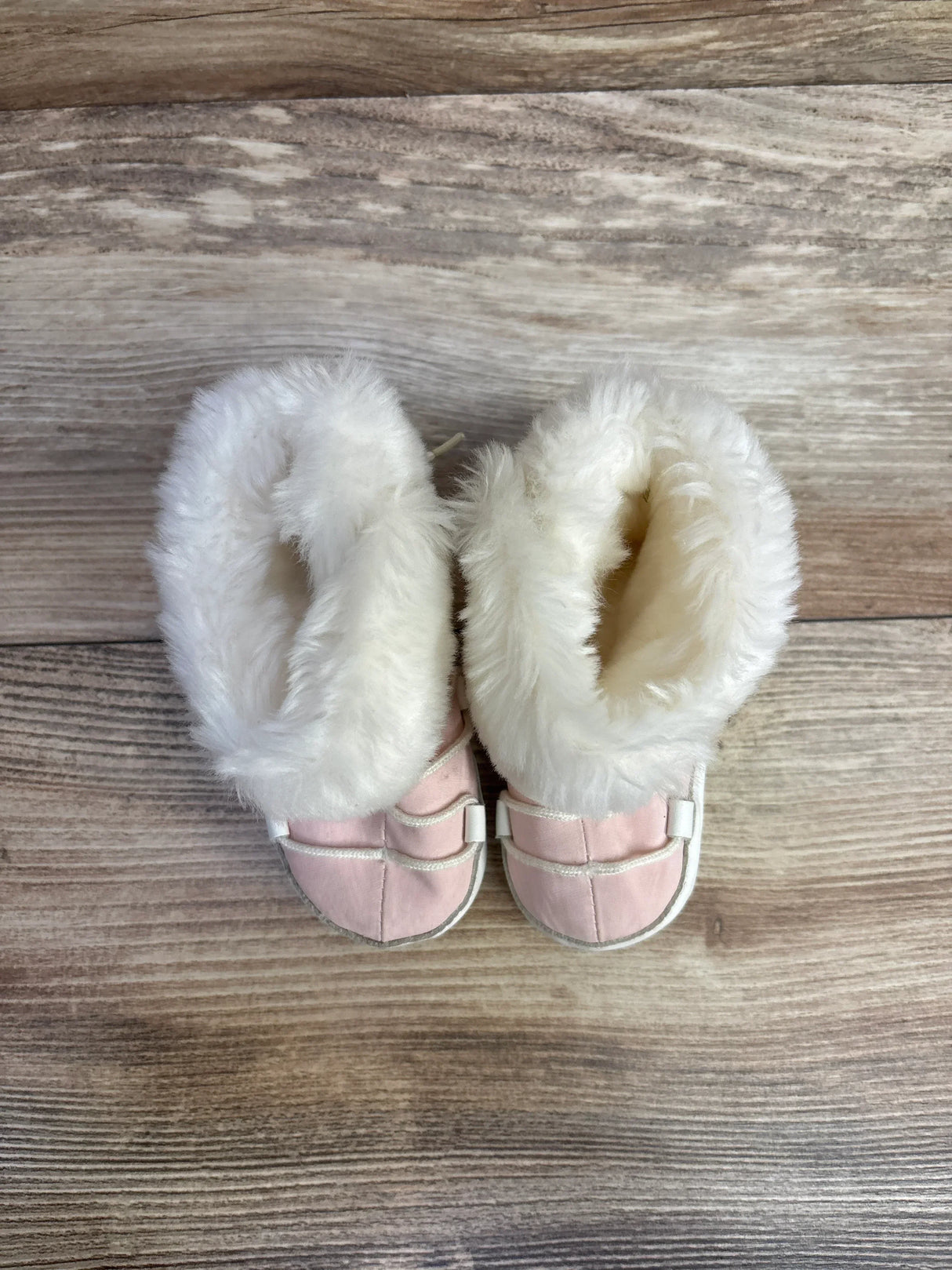 Pink baby booties with white faux fur on wood background
