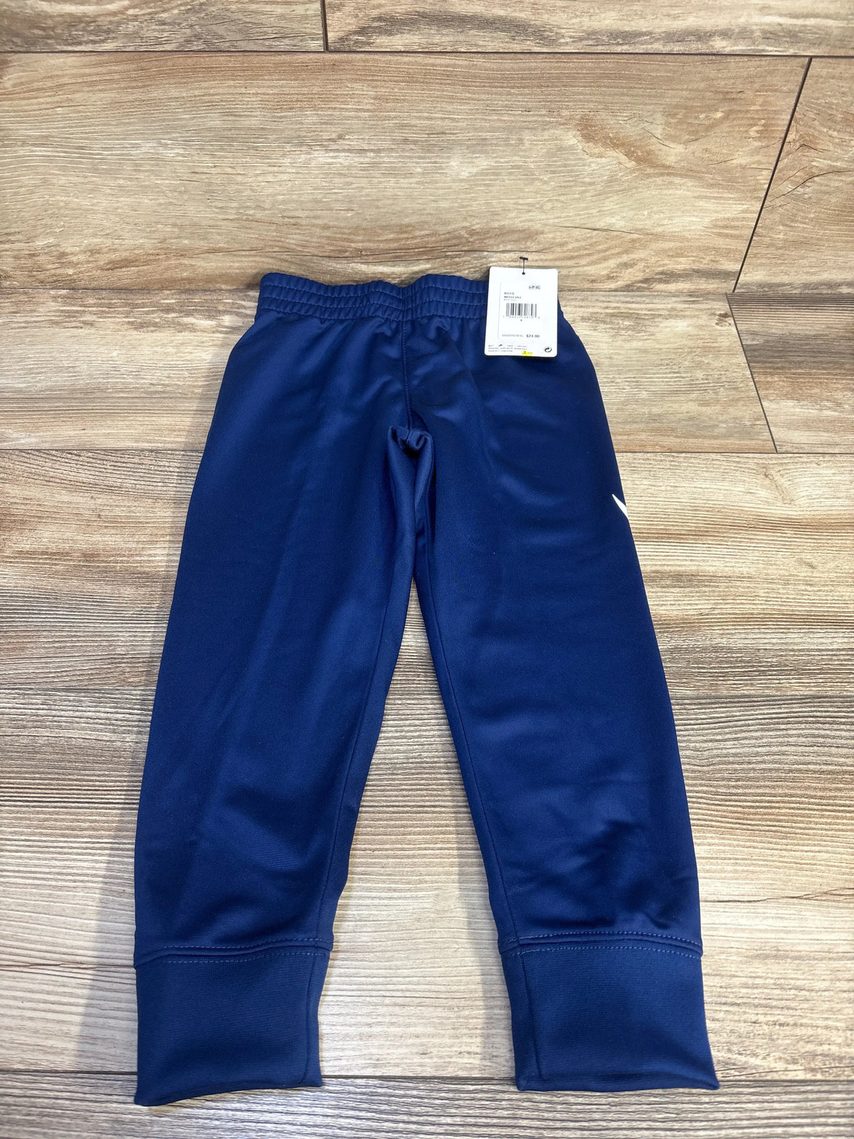 Front view of blue Nike Dri-Fit joggers in size 4T showcasing an elastic waistband and cuffed ankles on a wood floor
