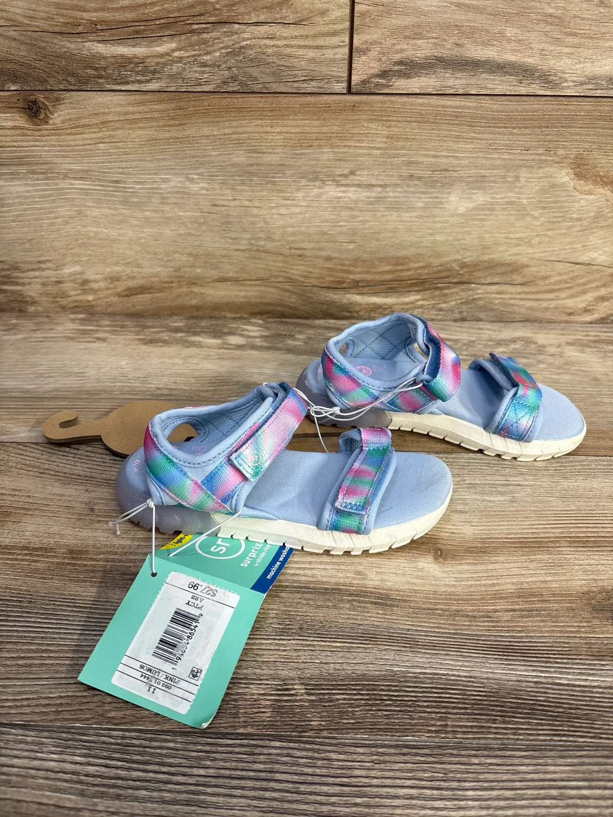 Top view of toddler light-up sandals with rainbow straps, blue footbed, white soles on wooden background, size 11C