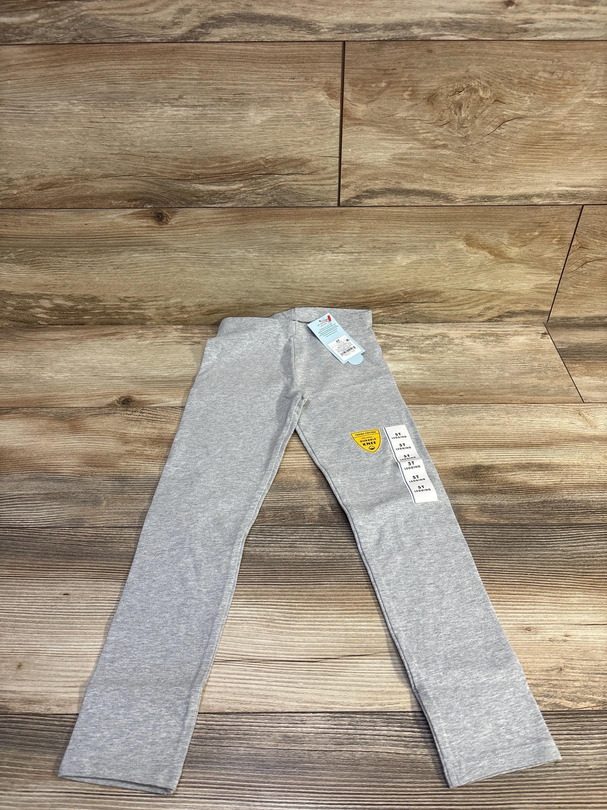 Flat lay of Cat & Jack grey toddler leggings size 5T showing full-length straight legs and elastic waistband on wood floor background