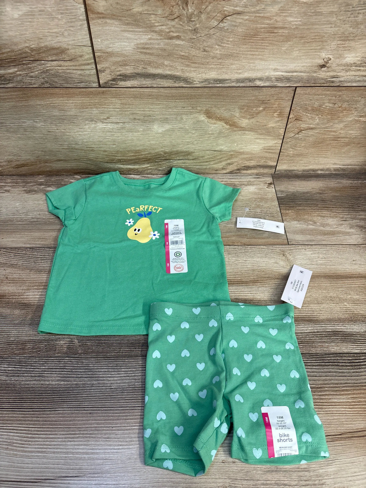 Front view of green Wonder Nation two piece shirt and bike shorts set showcasing pear graphic and heart pattern with wood background