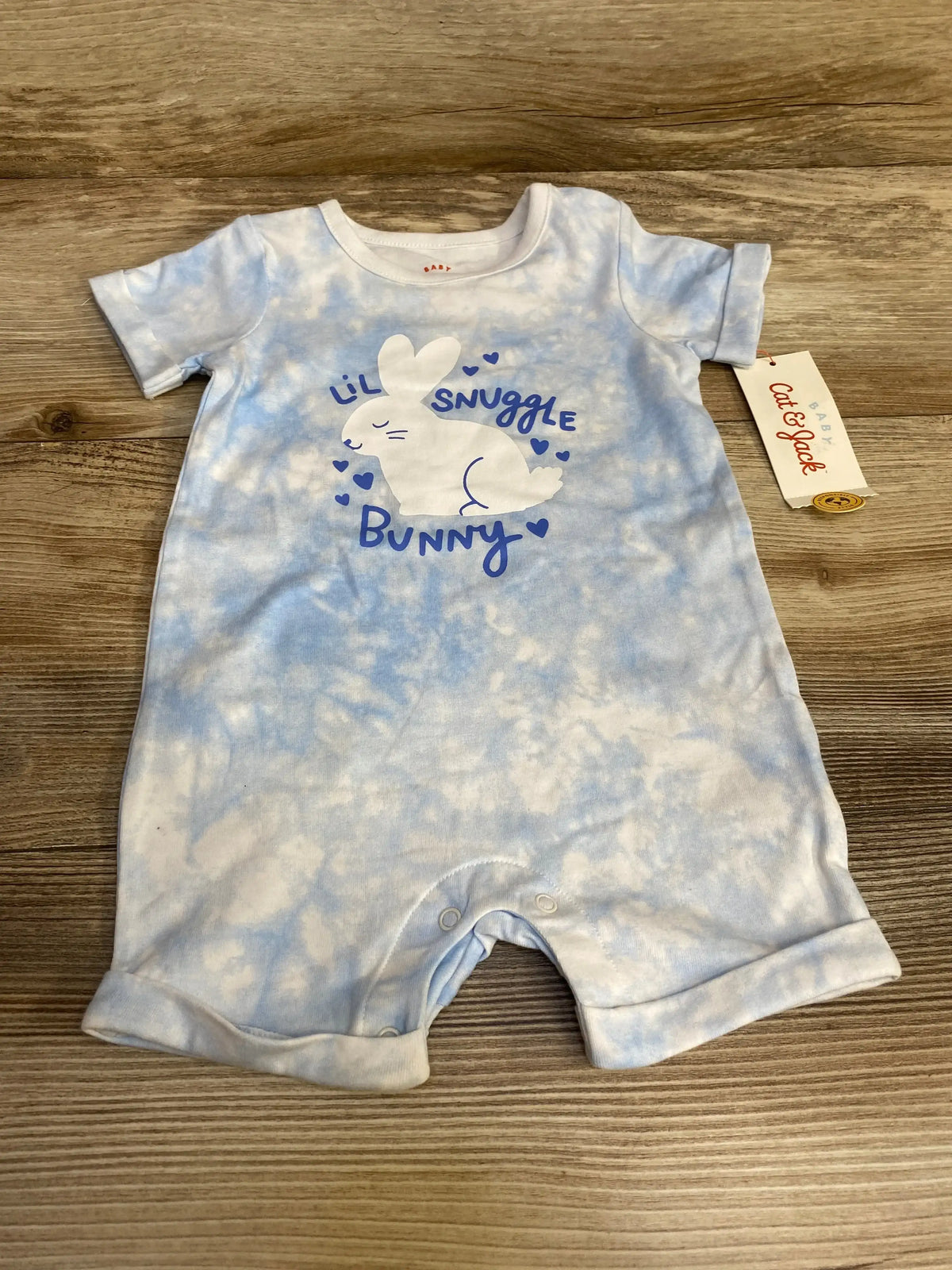 Flat-lay of Cat & Jack romper in light blue tie-dye showing white bunny graphic with ‘Lil Snuggle Bunny’ and snap crotch on wood