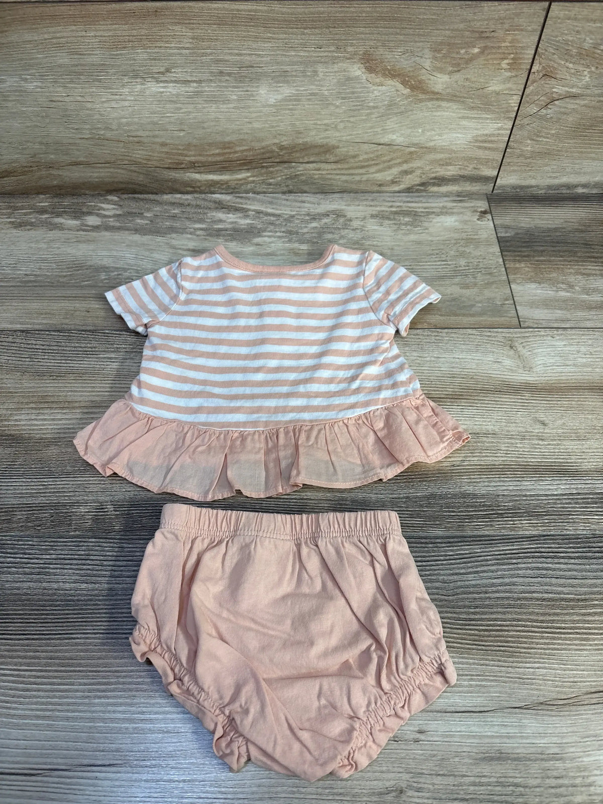 Flat lay of Peach Baby Gap two-piece set: striped peplum top with ruffle hem and matching bloomers on wood floor