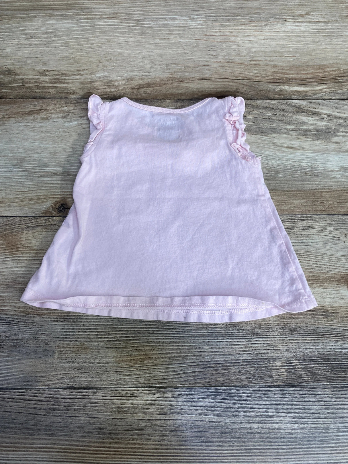 Back view of pink First Impressions eyelet ruffle baby shirt showing ruffled cap sleeves on wooden floor background