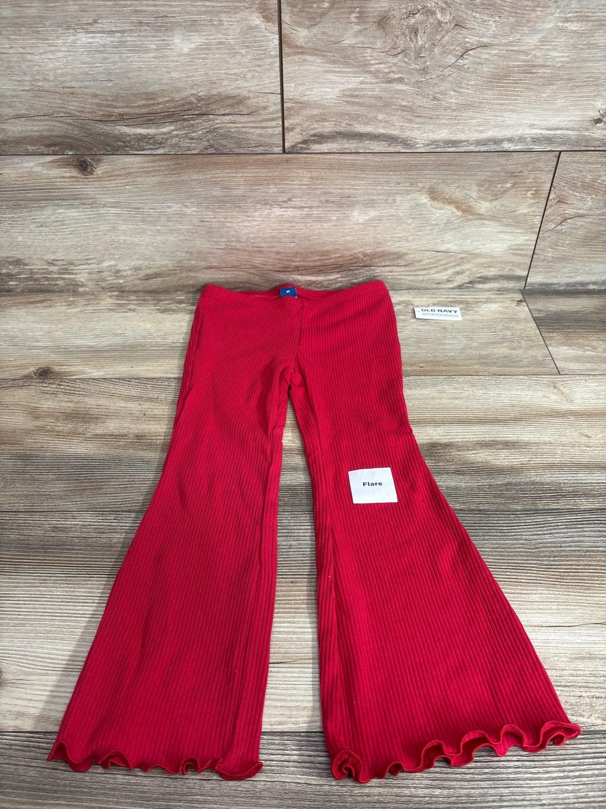 Top-down view of girls’ red Old Navy ribbed flare leggings showing flared legs and ruffled hem on wood floor background