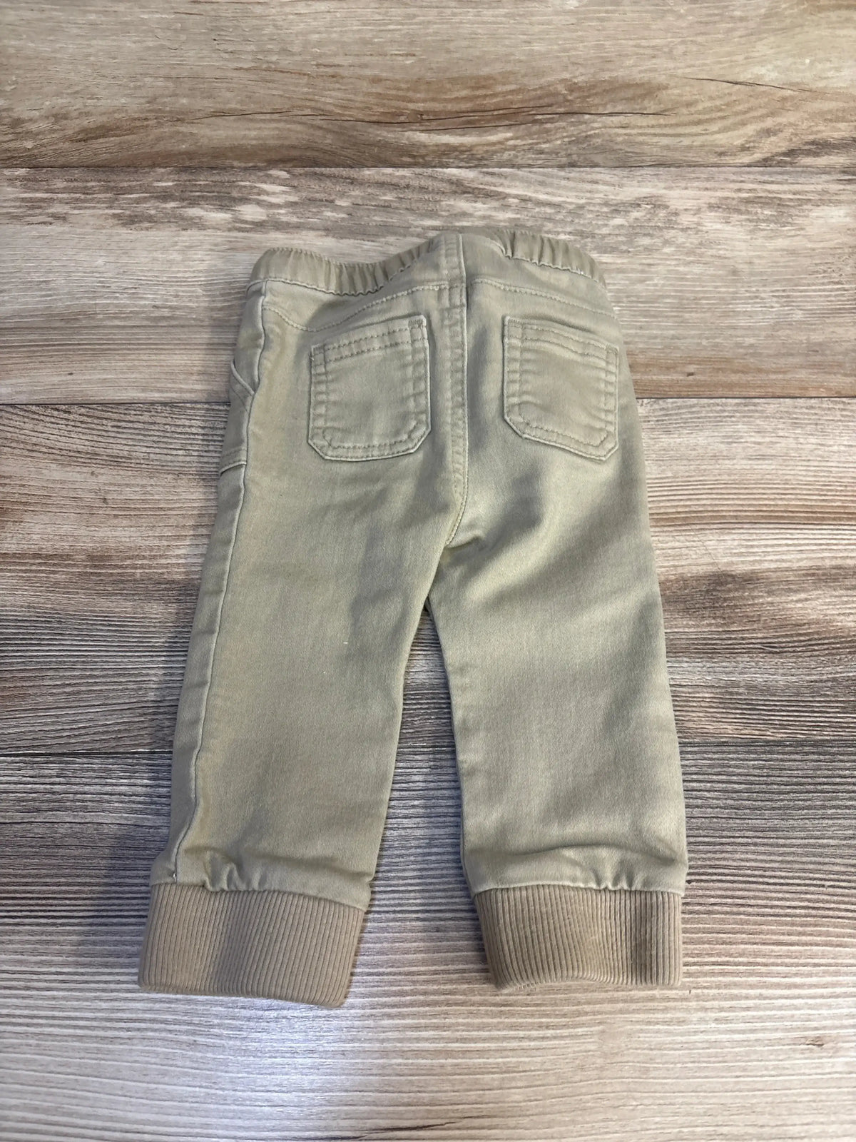 Beige toddler pants with elastic waistband and ribbed cuffs on wood background