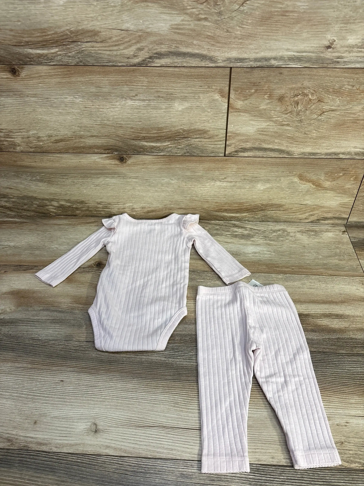 Flat lay of pink ribbed 2-piece bodysuit and leggings set showing ruffle shoulders and vertical ribbed texture on wood floor
