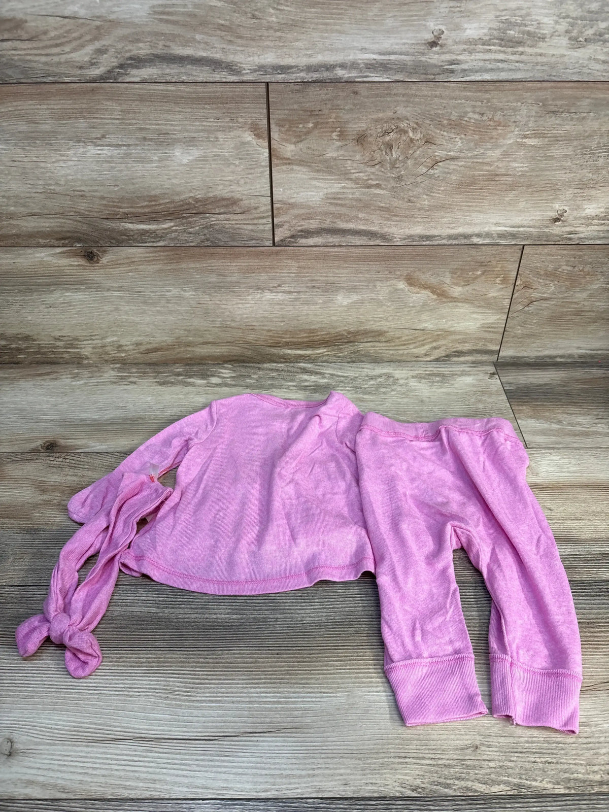 Flat lay of Cat & Jack hot pink infant ruffled long-sleeve top, matching pants, and knotted headband on wood floor