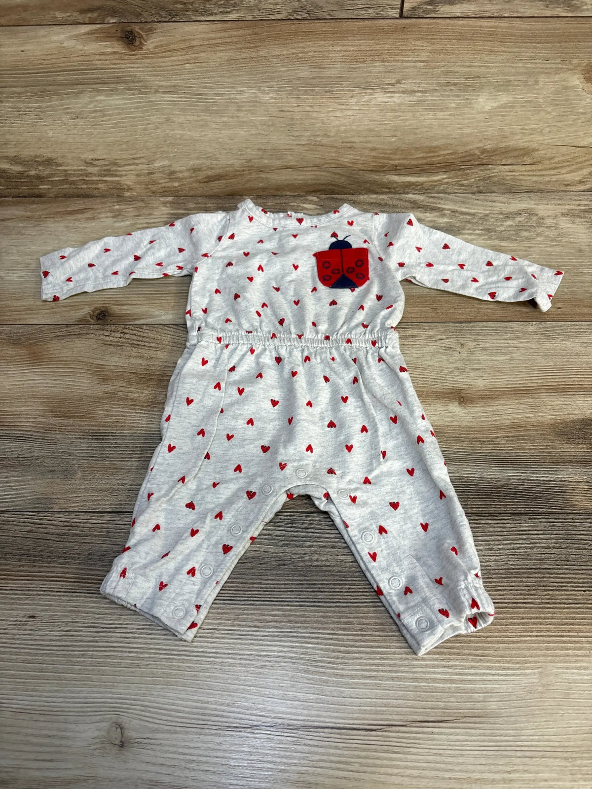 Grey baby romper with red heart pattern and ladybug patch, long sleeves, wooden floor background