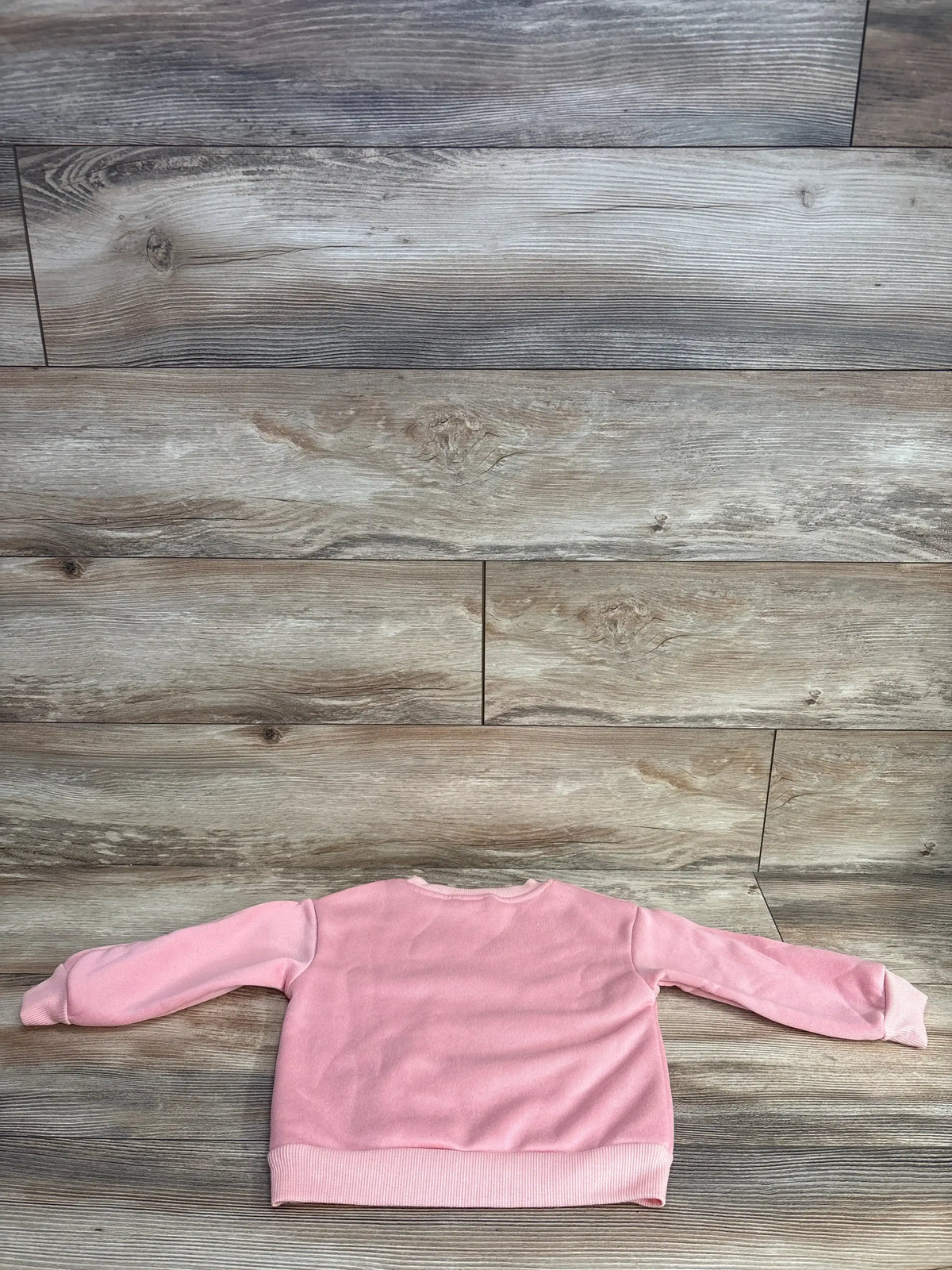 Pink toddler long sleeve sweater laid flat on wood floor, kids clothing resale