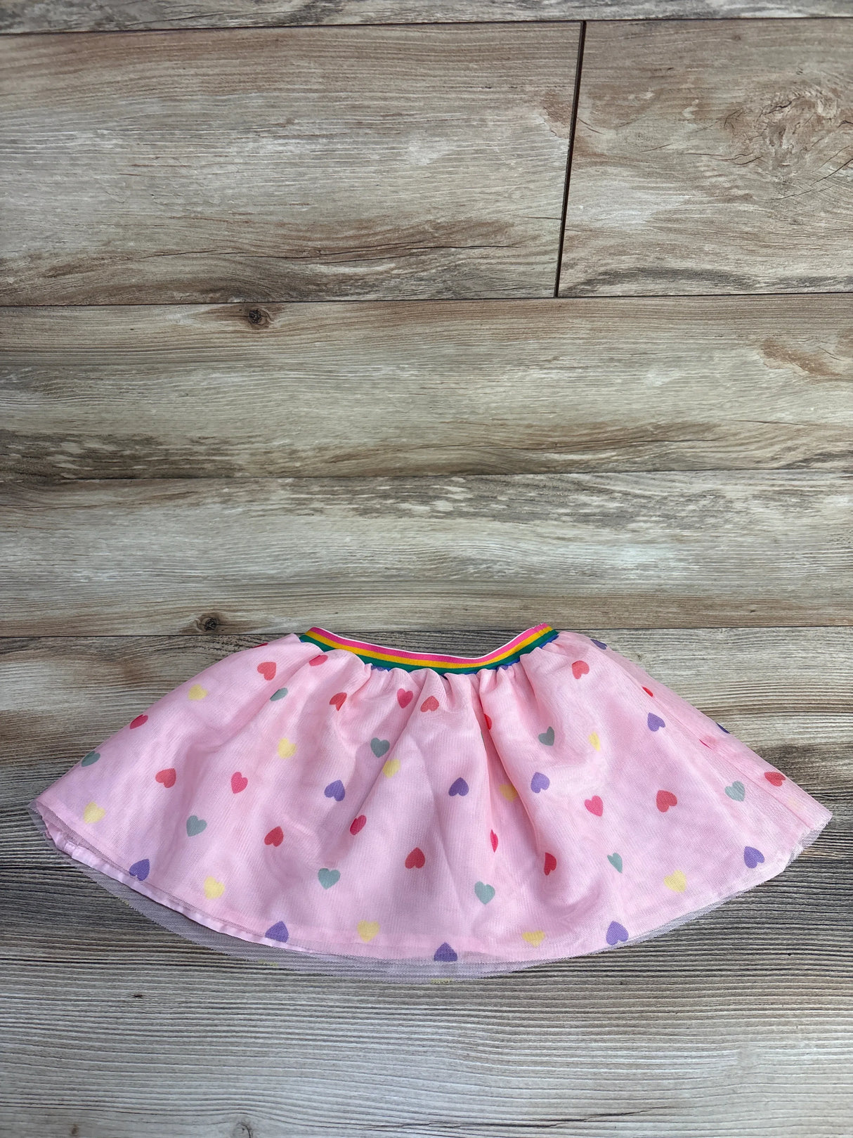 Pink toddler skirt with multicolored heart pattern and rainbow elastic waistband on wooden floor