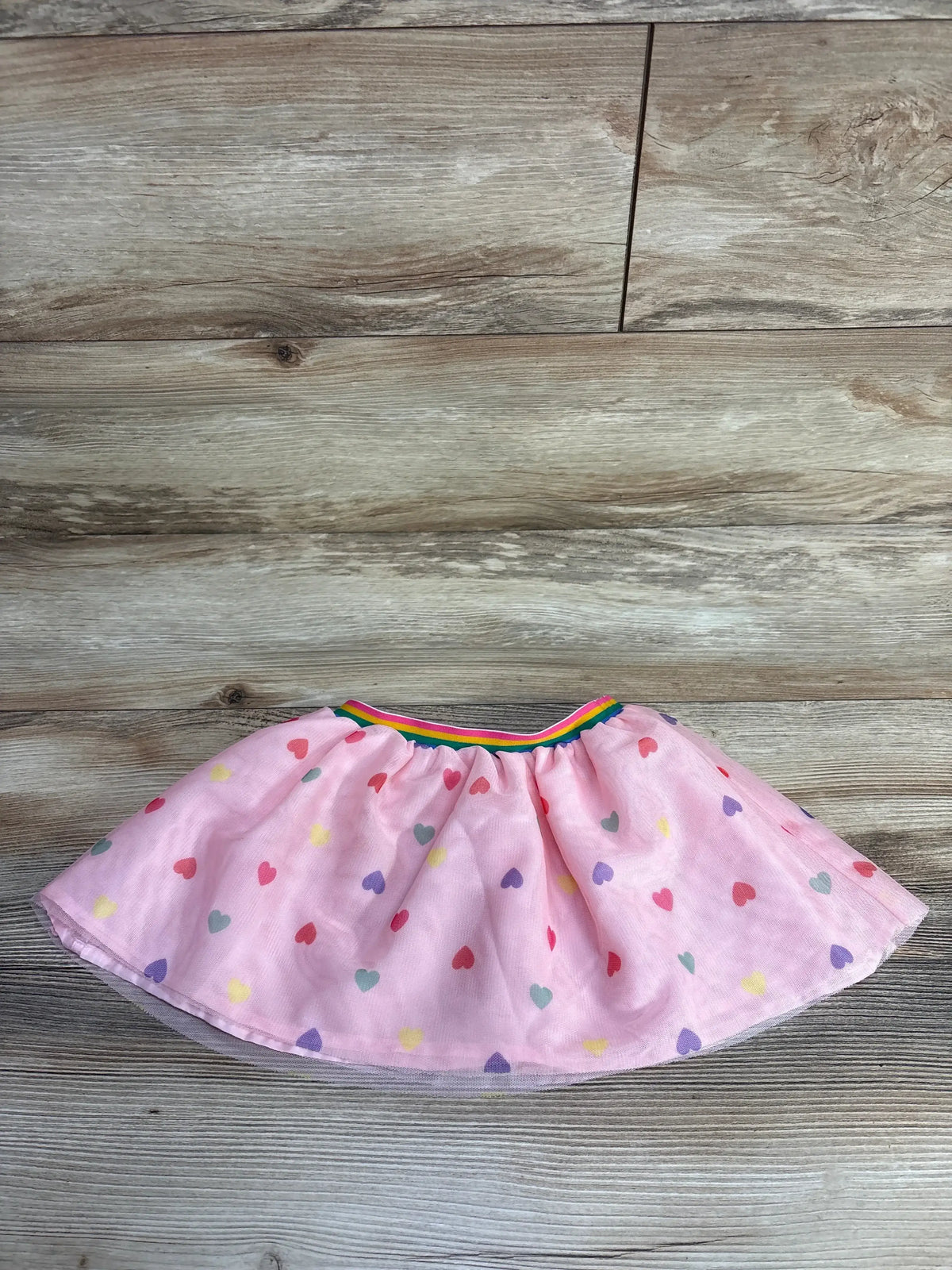 Pink toddler skirt with multicolored heart pattern and rainbow elastic waistband on wooden floor