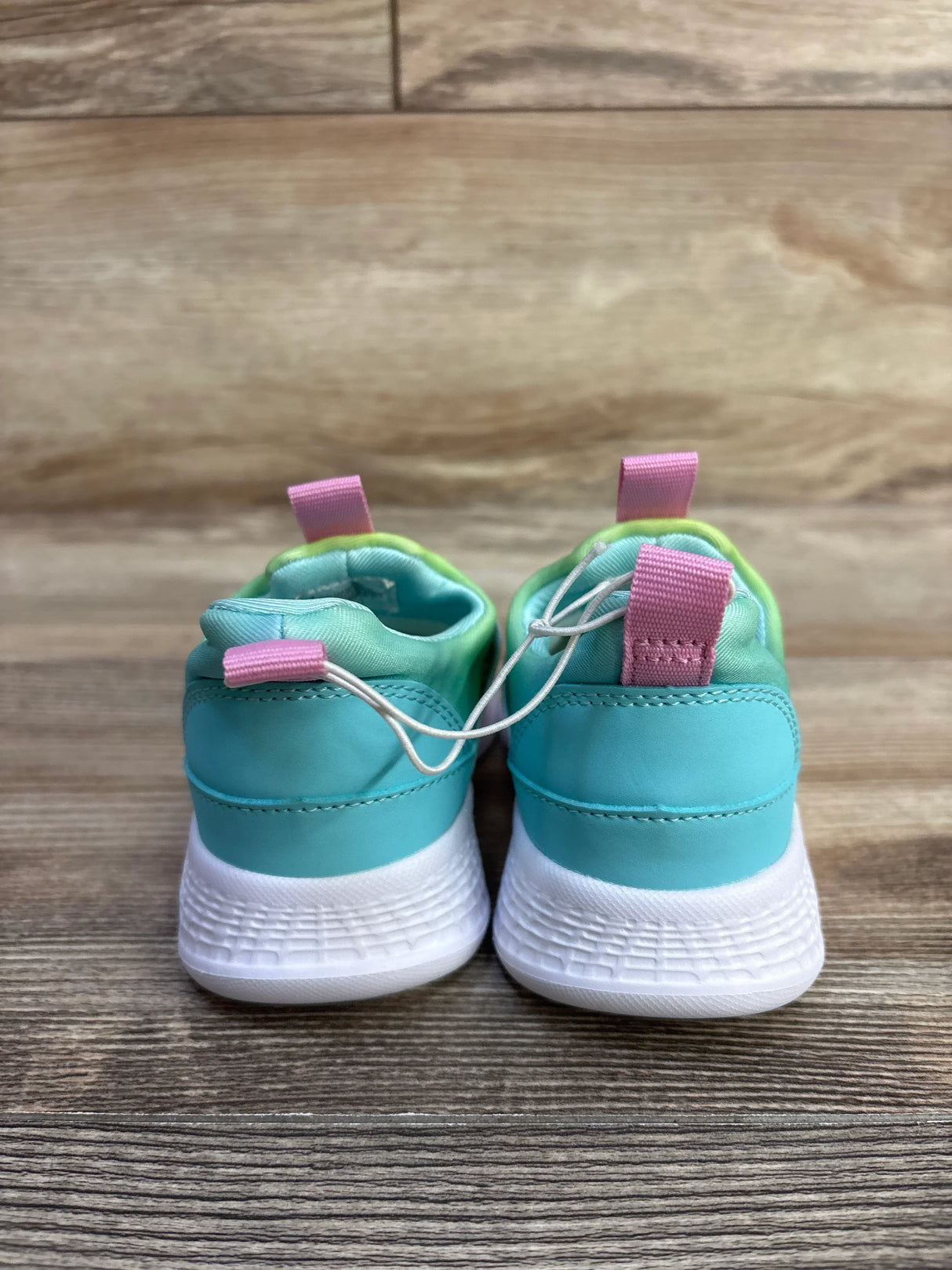 Rear view of Cat and Jack toddler slip-on sneakers with aqua upper, mint lining, pink heel tabs and white sole on wood floor