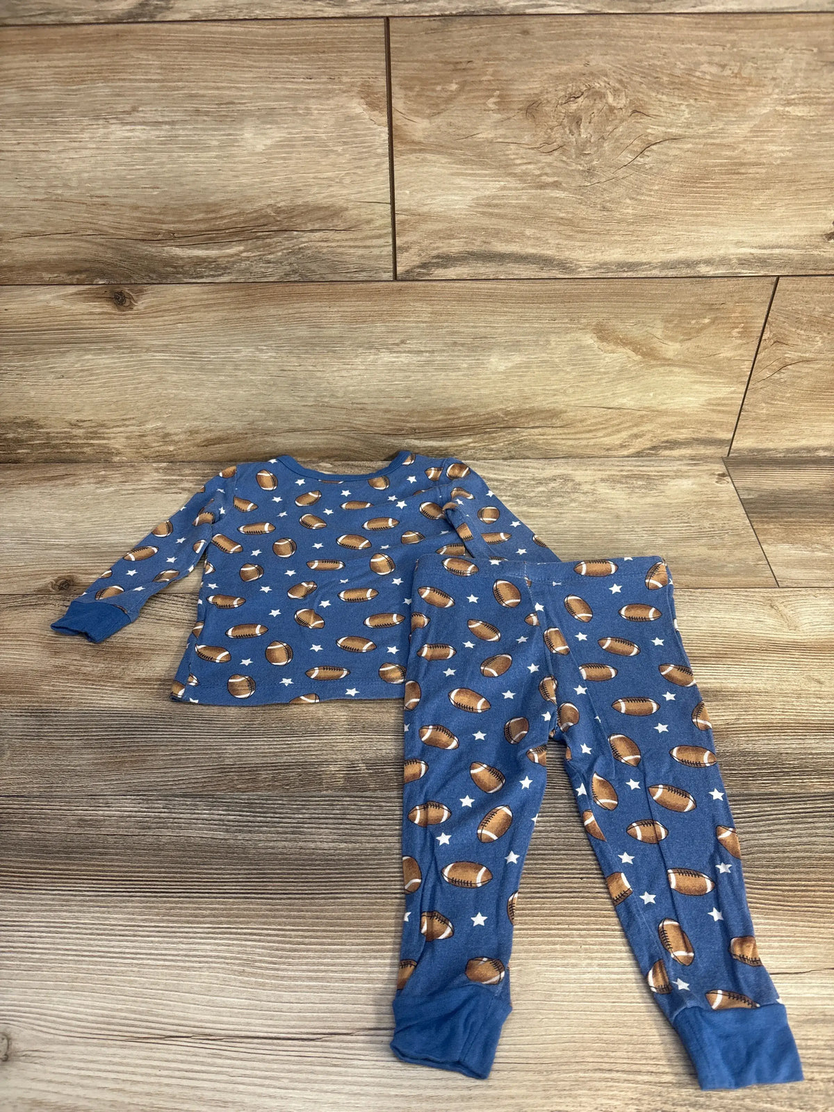 Flat lay of Little Me two-piece bamboo pajama set showcasing blue football and star print on a wood-look floor