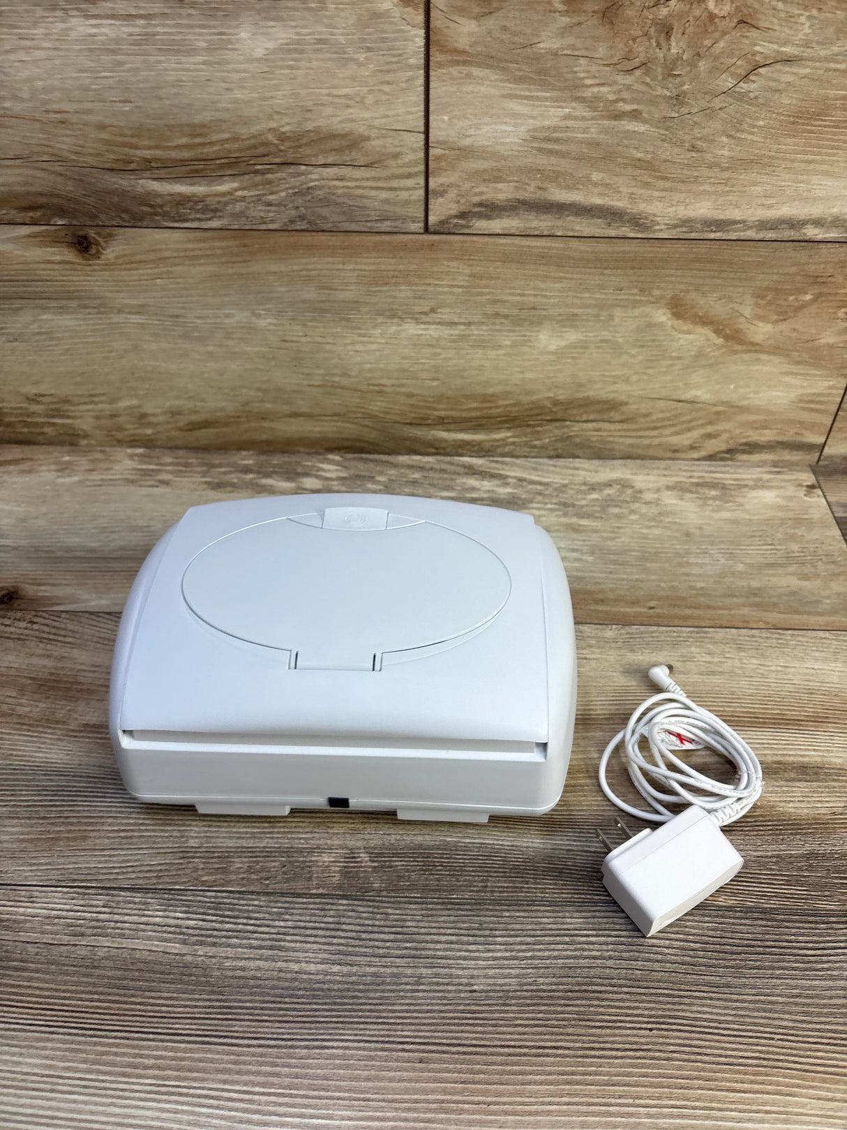 Angled top view of Prince Lionheart Ultimate Wipes Warmer showcasing the closed oval lid and included power adapter on a wood plank background