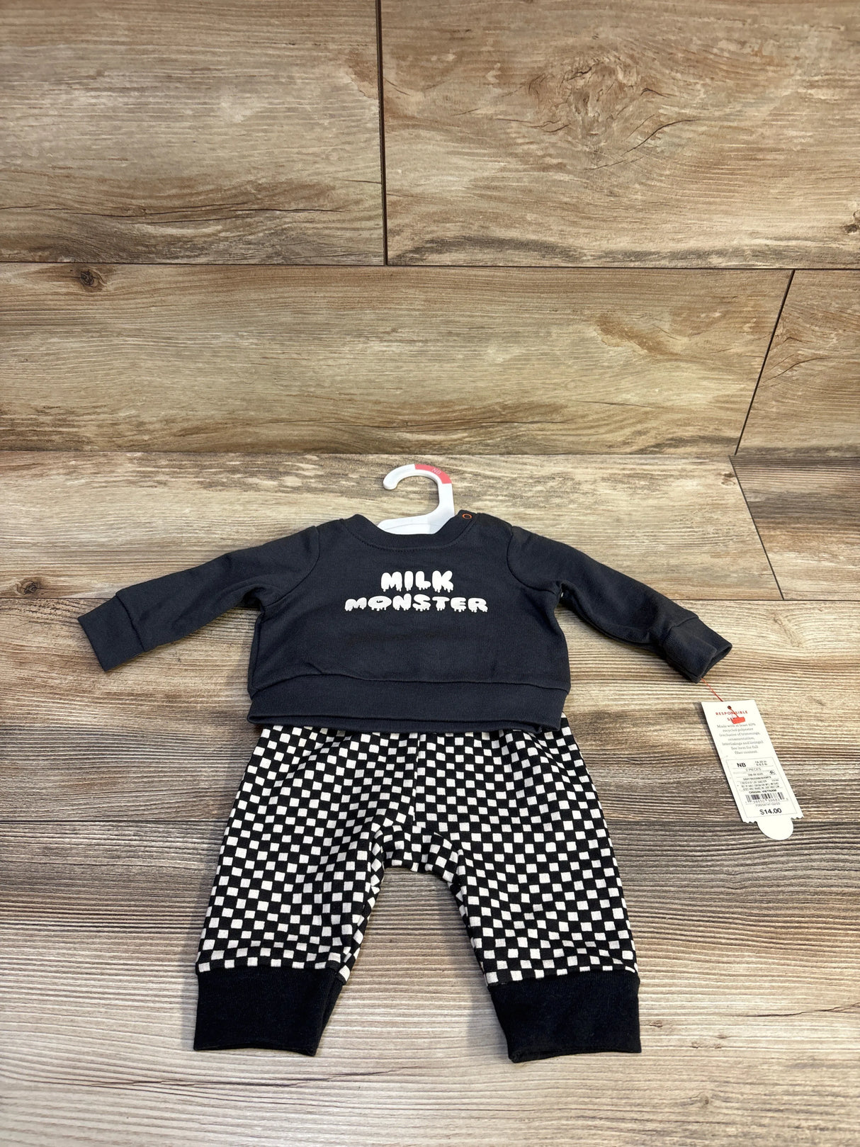 Flat lay of Cat & Jack newborn set with charcoal Milk Monster sweatshirt and black-and-white check joggers on wood backdrop